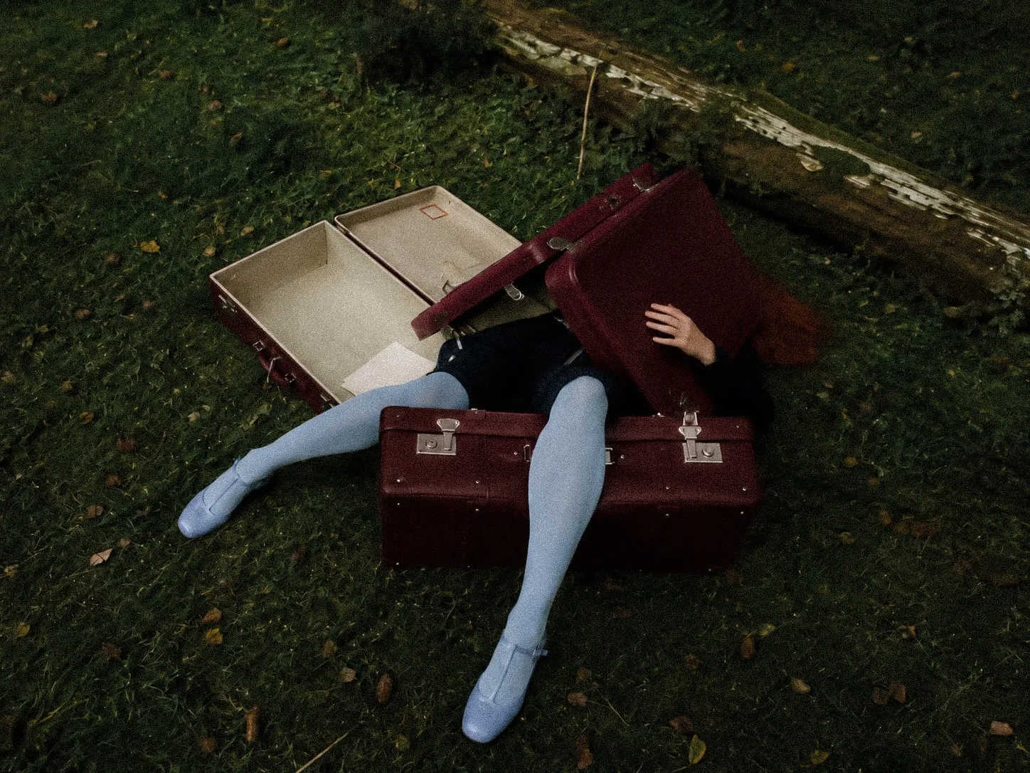 Anastasiia Preston lying in the grass among vintage burgundy suitcases